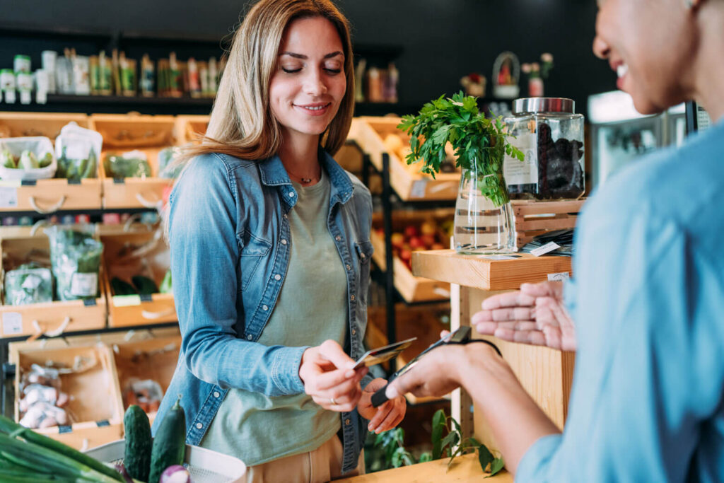 Customer paying with a card at a produce counter in a grocery store.